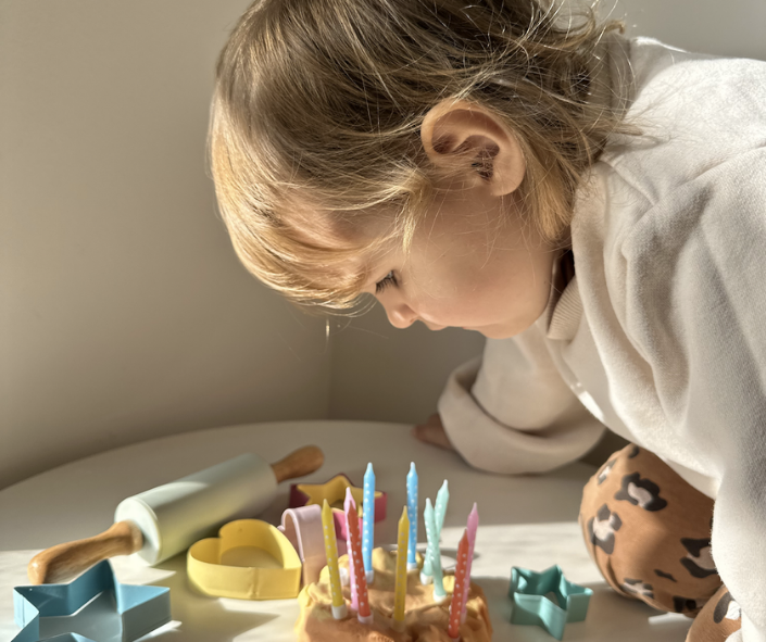 The girl is blowing out candles on the playdough cake.